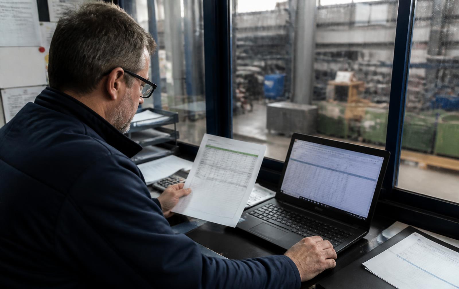 Manufacturing manager reviewing workforce cost figures in an office above the production floor